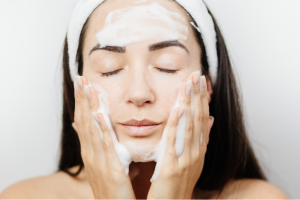 young-woman-cleansing-her-face-with-foaming-facial-cleanser-wearing-white-headband-gently-massaging-cheeks